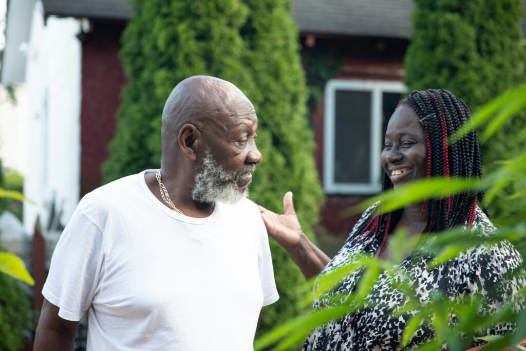 An older couple smiling at one another while outside surrounded by greenery
