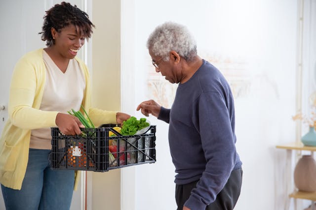 A young woman holding out a crate of vegetables to her grandfather