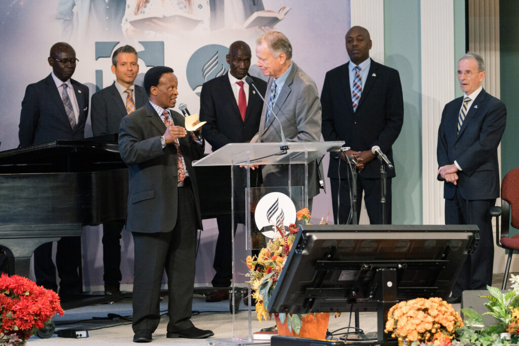 Adventist pastor Blasious Ruguri, president of the East Central Africa Division, speaking on a stage with Pastor Mark Finley